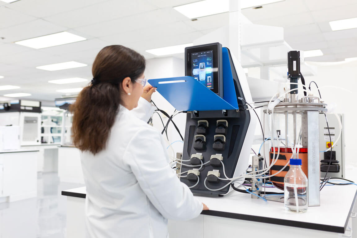 Scientist opening the front access panel of AUXO V benchtop bioreactor connected to fermentation vessels.