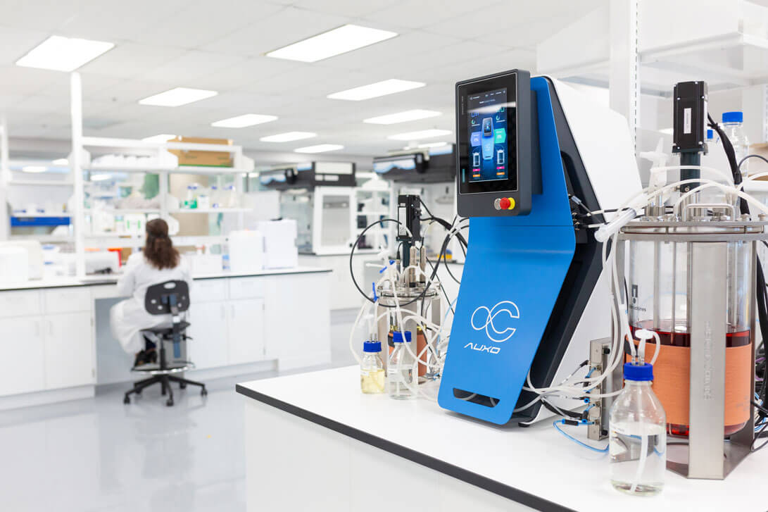 AUXO V benchtop bioreactor operating on a lab bench with connected vessels in a research laboratory.