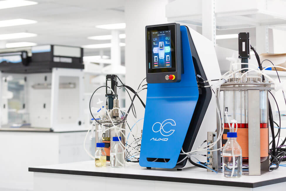 AUXO V benchtop bioreactor connected to bioprocess vessels on laboratory workbench.