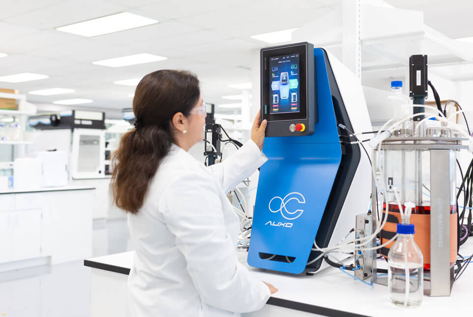 Researcher using touchscreen interface of AUXO V benchtop bioreactor in laboratory setup.