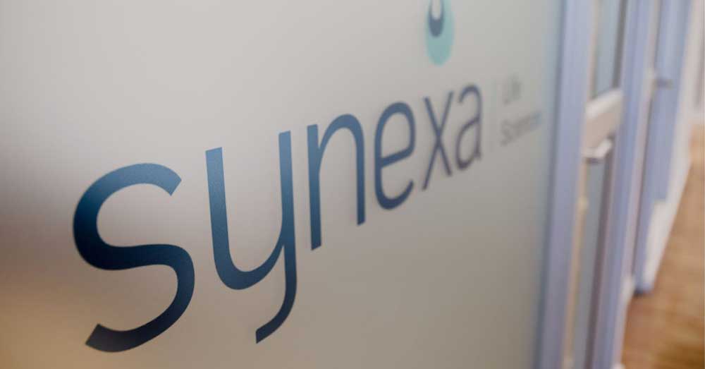Close-up of Synexa Life Sciences logo on frosted glass inside an office corridor.